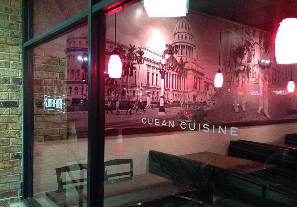 The dining room: a full-wall black and white photograph of Havana with CUBAN CUISINE letterspaced across it, the logo in window vinyl, warm pendant lighting
